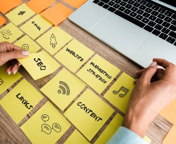 cropped view of woman touching sticky note with seo lettering near laptop on desk