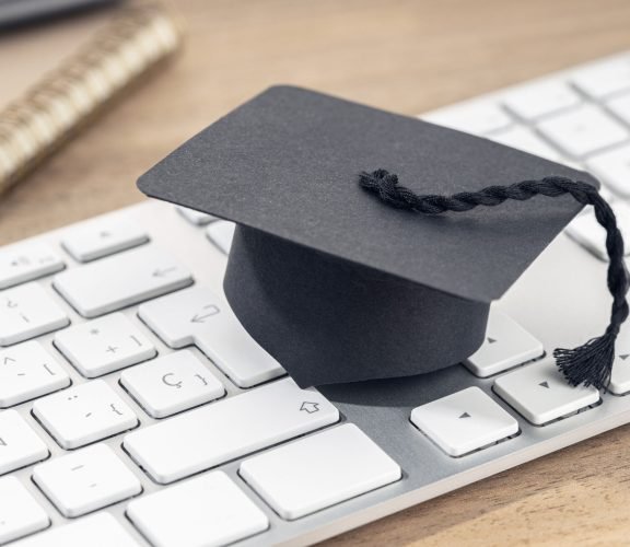 E-Learning or home study concept. Graduation cap on computer keyboard on wooden desk